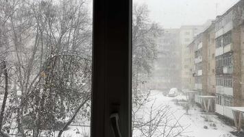 ordinario vida ventana de casa en Ucrania nieve invierno nieve copos que cae en desnudo arboles y suelo vida de real personas lento movimiento ver de calle desde calentar habitación calor es terminado frío tiene llegado video