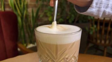 une femme est tournant une soucoupe et une verre avec une latté dans une café, sur le soucoupe mensonges une biscuit dans le forme de café des haricots video