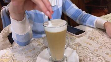 very long nails manicure pink gel polish false nails girl with cappuccino in a restaurant unrecognizable people hands drinking latte drink hot glass mug straw black. blue checkered sweater video