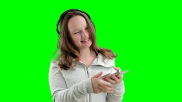 girl with her finger taps on professional headphones listen to music check quality in hands holds white smartphone mobile phone internet wi-fi on white background laughs smile makes eyes video