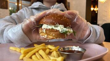 ung hungrig kvinna är bitande stor hamburgare. äter burger i snabb mat Kafé, närbild. video