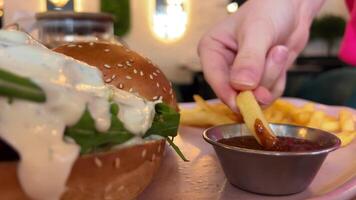 Closeup shot of dipping french fry into ketchup with hamburger in background. Shot on RED video