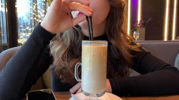 Cold coffee drink in a glass. Girl drinks morning coffee at a table in a cafe. video