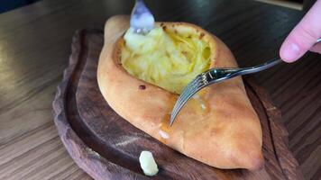 hand- menging ingrediënten van adjarian Khachapuri met vork in restaurant. Open brood taart met kaas en ei dooier. lekker Georgisch keuken. langzaam beweging. video