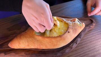 Hand mixing ingredients of adjarian khachapuri with fork in restaurant. Open bread pie with cheese and egg yolk. Yummy georgian cuisine. Slow motion. video