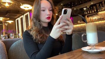 Fotografieren Glas von Latté Eis Mädchen im Restaurant Herstellung ein zum Sozial Netzwerke Trinken trinken Menschen hell rot Lippenstift schwarz Abend Kleid schick Platz zum Abendessen. Internet W-lan Sucht video