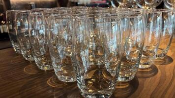 empty glasses neatly lined up on the sleek bar countertop. The crystal-clear vessels await the skilled hands of bartenders, ready to be filled with crafted libations . High quality 4k footage video