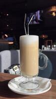 tazza di caffè nel bicchiere in piedi su di legno tavolo nel bar. foglia latte macchiato arte su caffè. vegano bevanda con soia latte nel caffetteria. 4k video