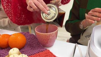 pouring chocolate tea, hot cocoa into a pink cup among a group of girls close-up teapot tangerines and candles Woman's hands brewing black tea tea party rest communication master class video