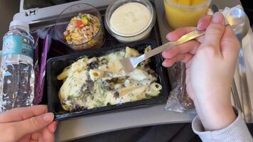 Inflight meal service tray for economy class, meat with pasta, seasoning fruit, salad, cucumber, a glass of juice and butter. selective focus. Pasta food on a plane video