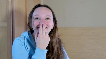 scratching nose upper lip thinking smiling girl sitting in room freckles no makeup dirty hair scratching lip thinking blue blouse sincere emotions interest curiosity video