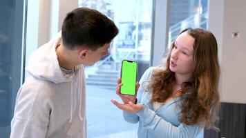 Young millennial friends sitting outside with coffee and looking at green screen phone in park. Happy smiling people using modern smartphone technology. Media, lifestyle, internet education concept video