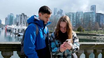 boys girl stand Pacific Ocean with ships take a selfie look diligently into the phone skyscrapers bridge blue color in clothes backpack brother sister tourists couple friends together video