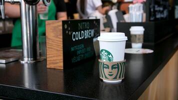 Starbucks preparing coffee of various drinks behind counter women white t-shirt aprons and masked sellers in glasses of Asian-European ethnicity girl peeking in to take coffee latte showcase issuance video