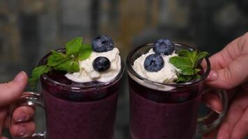 Party for two sweets in a glass glass two hands take blueberry dessert with mint and vanilla with cream and fresh blueberries in different directions space for text advertising video