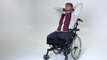 adult man is sitting in wheelchair with hands behind head he raised head up dreams of remembering past Ukrainian embroidered shirt with red embroidered on white corrects itself in chair Ukraine video