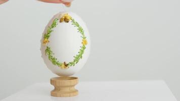 närbild av ett broderad ägg på de äggskal av gås ägg kvinna hand långsamt sätter den på en trä- stå på en vit bakgrund krashenka ritningar ornament landskap påsk firande video