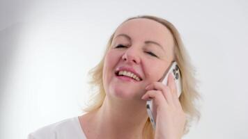 Pretty blond woman listening to a call on her mobile phone smiling at the news head and shoulders in front of white curtains video