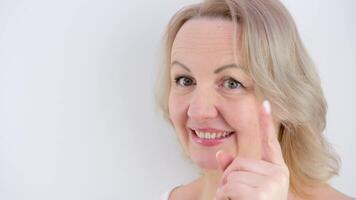 woman shakes head negatively with smile she came up with raised finger put finger to chin squint eyes smile on white background space for text advertisement tenderness beauty self care great idea video