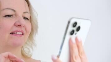 a woman touches the monitor screen looks at a mobile phone news social networks internet communication new s on a white background close-up white phone three cameras video