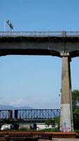 pattulo brug over- fraser rivier- trein voorbijgaan onder brug. detailopname schot van technologisch plaats verspreide ijzer balken voor de bouw van nieuw brug tegen de backdrop van bergen en lucht video