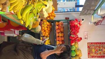 granville isla un asiático mujer en un máscara con un delantal y un azul camiseta mira a el lista ese ella necesidades a comprar a el tienda de comestibles bazar ella toma bananas desde el mercado y pone su bolso abajo video