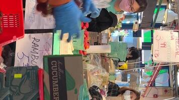 Granville Island In the market a seller a man in blue gloves puts lychee into a bag He packs them by the kilo Lychee brought in red containers Customers in the background video