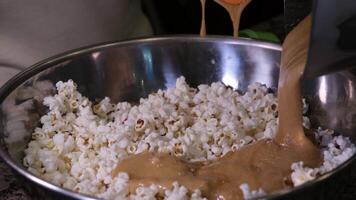 cooking popcorn at home in a special machine caramel filling caramelized popcorn recipe close-up delicious treat for movie stir and pour caramel icing popcorn grains iron utensil appetizing snack video