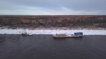 Visualizza a partire dal un' elicottero.clip. un' primavera paesaggio dove grande navi esportare carico lungo il fiume Il prossimo per spoglio leggermente nevoso foreste. video