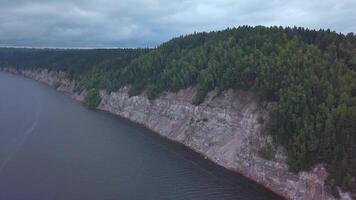 Aerial view of the steep cliff above the calm river surface. Clip. Green pine tree forest on hills and water surface. video