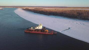 A ship carrying cargo. Clip. Ships sailing in a spring melting river with a large cargo against the background of forests with snow around and blue sky above. video