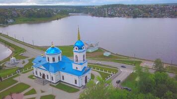 Aerial view of the city located in picturesque area on a summer day. Clip. A church with the blue roof, a pond and city houses far in the distance with the forested mountains on the background. video