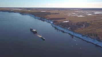 aéreo ver de un barcaza flotante en un amplio río pasado el otoño prados acortar. el carga Embarcacion que lleva bienes a un navegable río. video