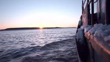 vue de le bateau. agrafe. une bateau avec une petit montant de neige sur il flottant vers l'avant sur lequel le vagues de le rivière Pause une part et de au loin vous pouvez voir le sortant brillant Soleil et le forêt. video