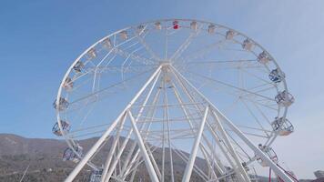 A ferris wheel at the amusement park at daytime. Action. Bottom view of white romantic attraction on blue sky background. video