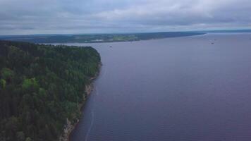 Aerial view of the steep cliff above the calm river surface. Clip. Green pine tree forest on hills and water surface. video