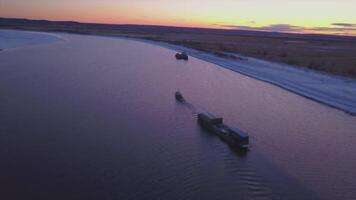 Cargo transport ship sailing on a wide river at summer dawn. Clip. Aerial view of the barge floating along the endless field towards the sunset, concept of water transport. video