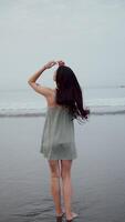 Girl stands back against the ocean and waves, running towards the camera smiling video