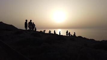 4k di un' gruppo di persone godendo il tramonto al di sopra di il mare a partire dal il scogliera. video