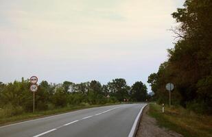 Empty asphalt road and floral field of different grass and flowers in evening time photo