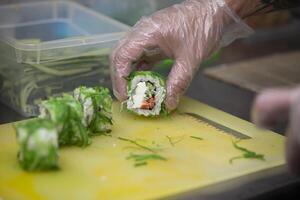 un enguantado mano cortes Sushi en un corte tablero. foto