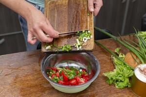 picar el verde cebollas y Tomates y sitio ellos en un bol. preparar el ensalada. foto