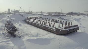 Aerial view of an old pier and a moored rusty ship on a snow covered shore. Clip. Winter landscape of an abandoned pier and a vessel on the background of cranes and construction site. video