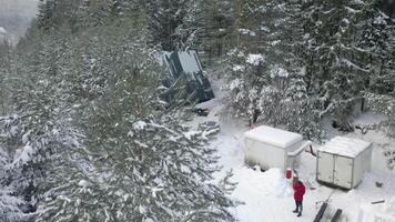 aéreo ver de un invierno acampar situado profundo en invierno bosque y un masculino caminante en calentar ropa. acortar. pequeño casa construido entre nieve cubierto abeto arboles video