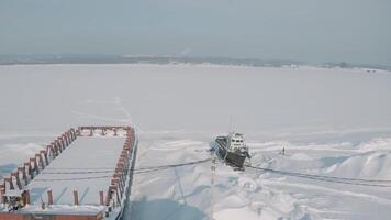 aéreo ver de un antiguo muelle y un amarrado oxidado Embarcacion en un nieve cubierto costa. acortar. invierno paisaje de un abandonado muelle y un buque en el antecedentes de grúas y construcción sitio. video