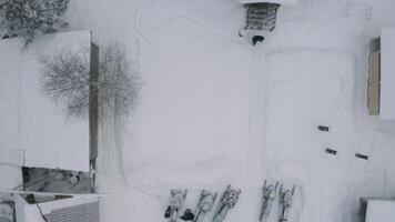 Antenne oben Aussicht von ein schneebedeckt Hof mit klein Häuser und geparkt Schnee Handys und Autos. Clip. Dächer von Gebäude bedeckt durch Schnee und ein Gehen Mann. video