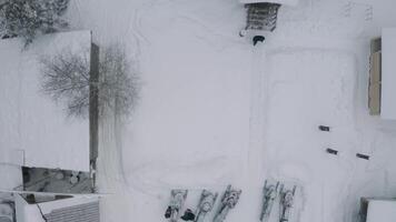 Aerial top view of a snowy courtyard with small houses and parked snow mobiles and cars. Clip. Roofs of buildings covered by snow and a walking man. video