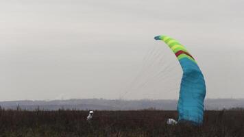 skydiver è atterraggio su il erba campo. azione. autunno paesaggio con un' atterraggio paracadutista con un' montagne e nuvoloso pesante cielo su il sfondo. video