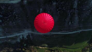 Aerial top view of a red hot air balloon floating over a mountain slope, a narrow path, and a green meadow. Shot. Concept of travelling and adventure. video