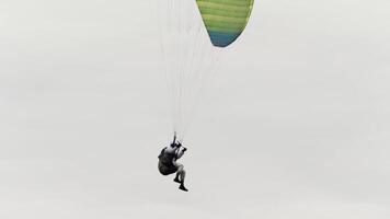 paracaidista es yendo a tierra y terminar su vuelo. acción. fondo ver de un aterrizaje paracaidista con un nublado pesado cielo en el antecedentes. video